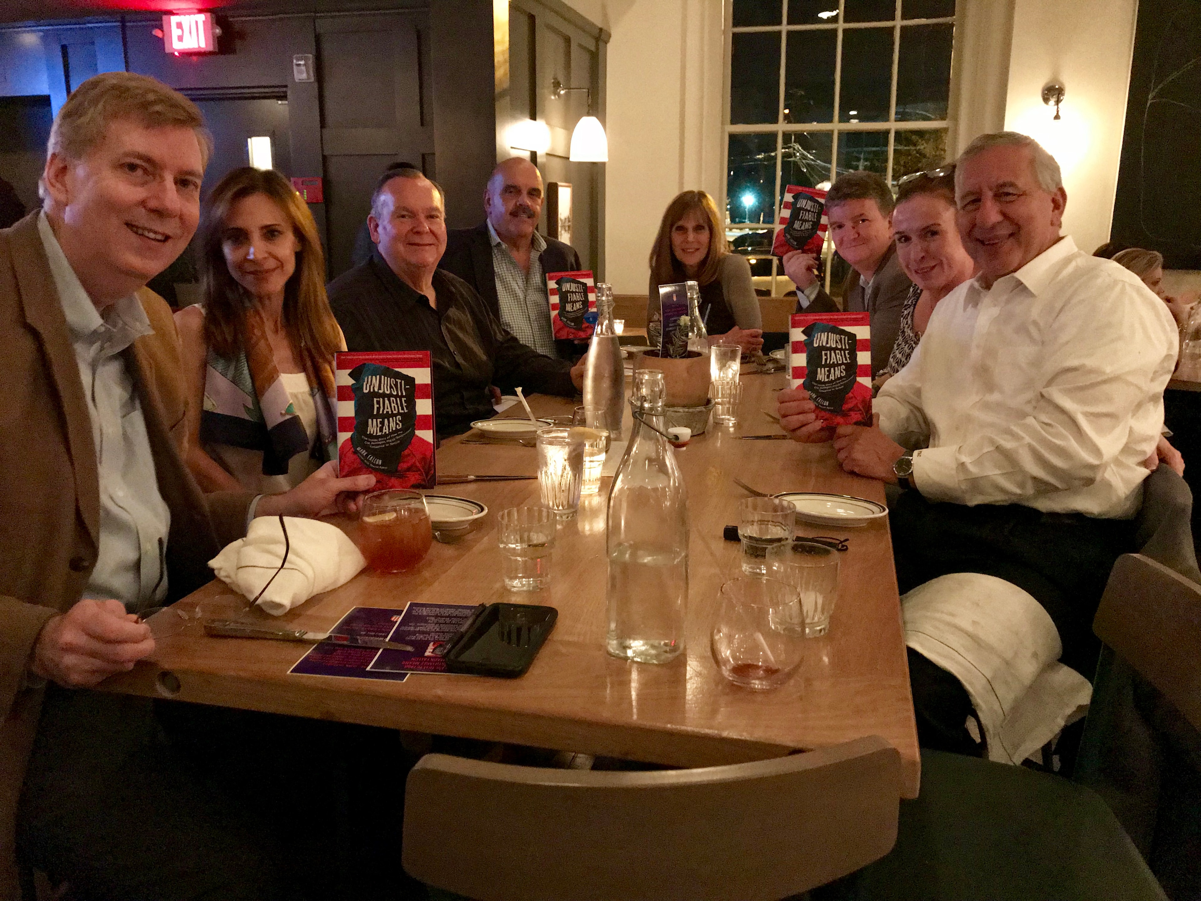 A group of supporters and friends gathered at a dinner table, each holding a copy of Unjustifiable Means