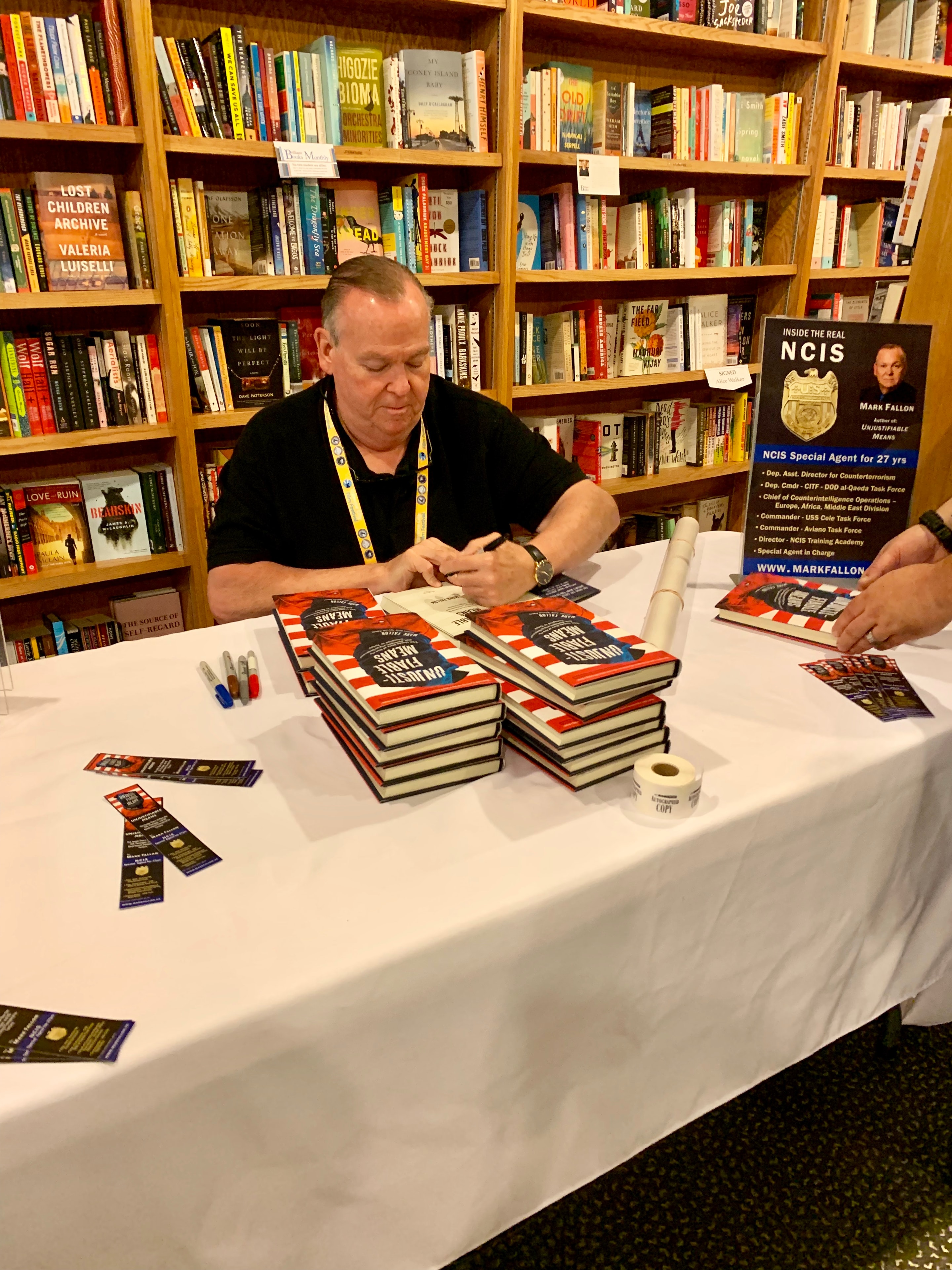 Mark Fallon signing copies of Unjustifiable Means at a bookstore with stacks of books on the table