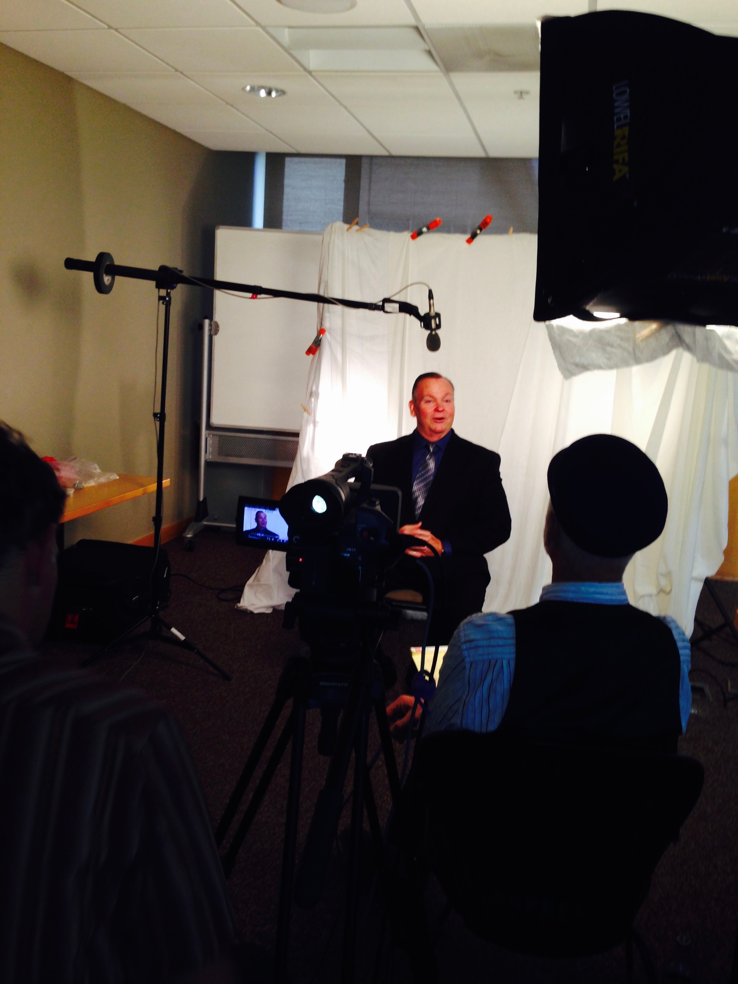 Mark Fallon being filmed in a makeshift studio with camera crew and boom mic