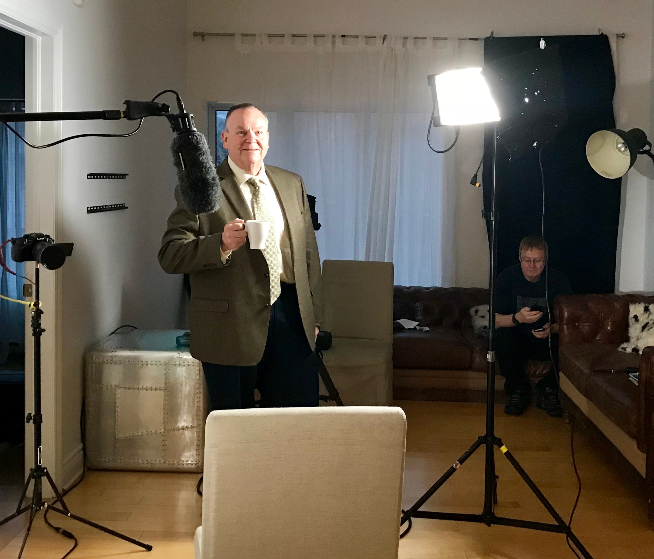 Mark Fallon on set between takes, holding a coffee cup surrounded by film equipment